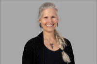 Business headshot of woman with white hair in dark top on gray background.