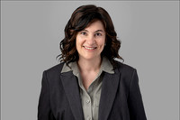 Studio portrait of woman with curly hair in blazer, gray background.