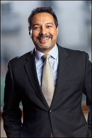 Smiling male executive in a dark suit and tie with a clean, modern background.