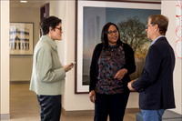 Three professionals in conversation in a corporate office hallway during a headshot session.