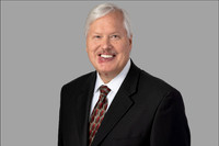 Corporate headshot of older man in suit with soft gray background.