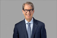 Headshot of smiling man in glasses and blue blazer on neutral background.
