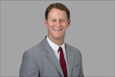 Professional headshot of smiling man in light gray suit on gray background.