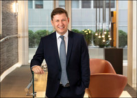 Corporate headshot of man in suit with modern interior background.