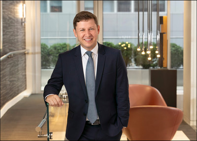 Corporate headshot of man in suit with modern interior background.