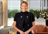 Corporate headshot of woman in black top with warm interior background.