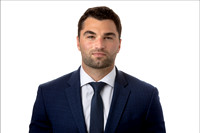 Headshot of man in blue suit with white background.