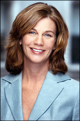 Professional headshot of a woman in a light blue blazer smiling, blurred office background, clean light.
