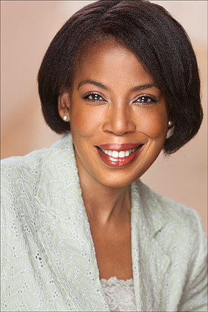 Portrait of smiling Black woman in light green jacket with soft background, classic corporate headshot.