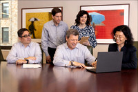 Group of professionals gathered around a laptop in a casual corporate meeting.