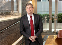 Executive headshot of man in suit with office hallway backdrop.