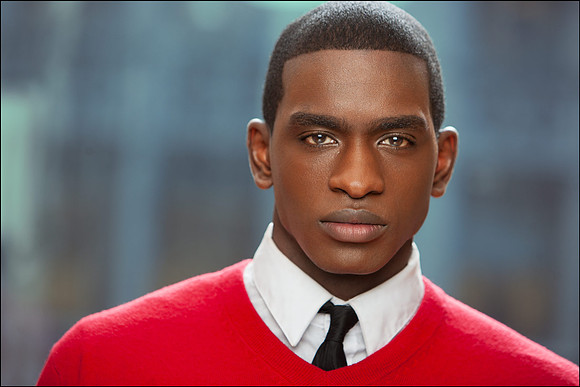 Professional NYC headshot of young Black man in red sweater and tie, stylish and strong