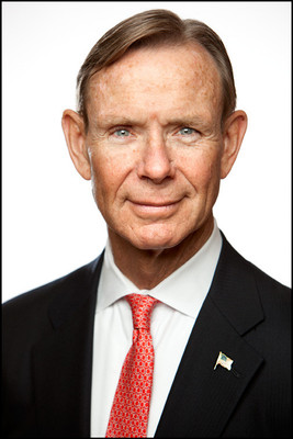 Professional headshot of senior male executive in suit and red tie with American flag pin, white background.