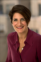 Woman in a maroon blazer smiling in a professional headshot with clean light and soft background blur.